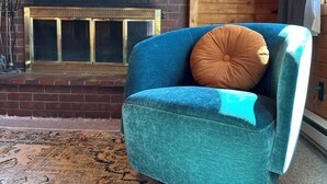 A cozy room with a blue armchair, a fireplace with a painting above it, and a patterned rug on the floor. - Entire Cabin: Step Back in Time at The Piney Lodge (Grand Lake)