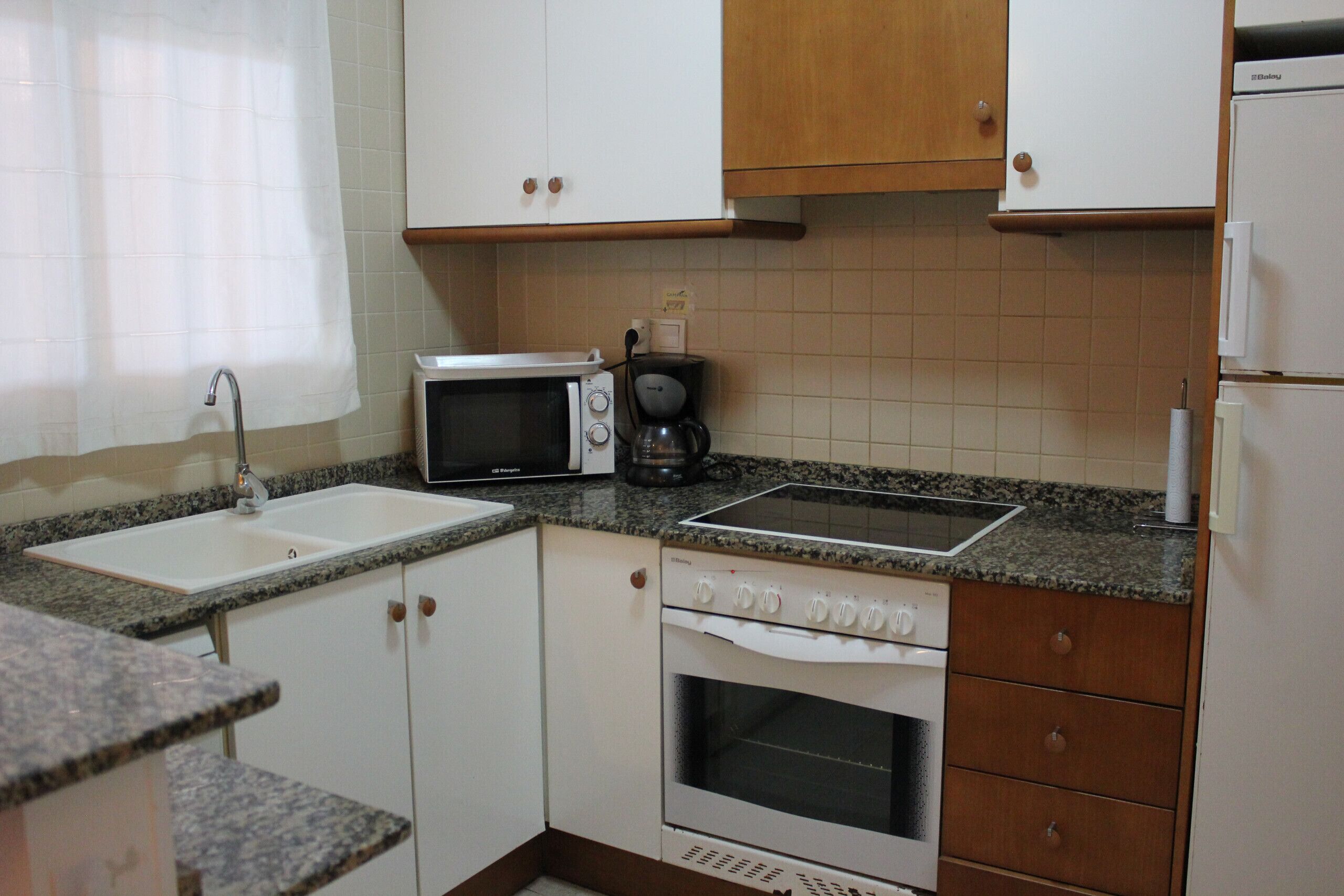 Eine Küche mit Mikrowelle, Kaffeemaschine, Herd, Backofen und Spüle.