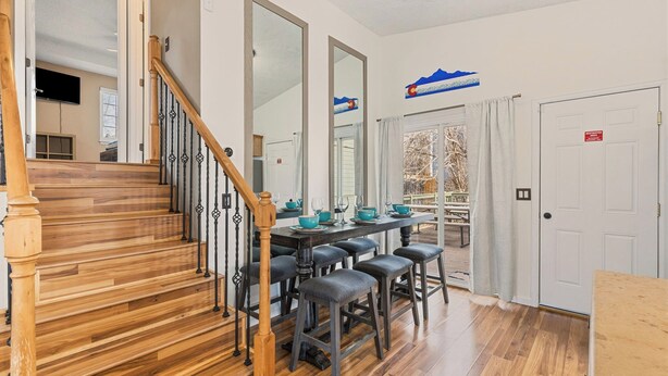 Un espace repas agrémenté d’un escalier en bois, d’une longue table avec des tabourets de bar et offrant une vue sur l’extérieur.