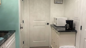 A narrow hallway with a white door, a trash bin, a coffee maker, and a sign on the wall. - Excellent location! Close to Famous Boardwalk. One block from the boardwalk. (Wildwood)