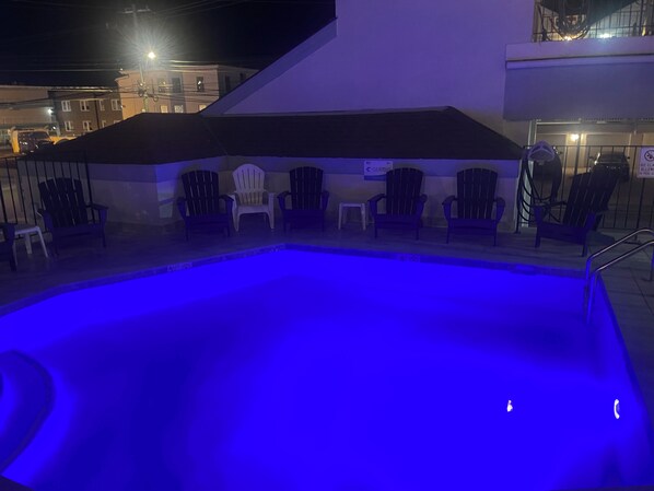 A swimming pool with a blue light, surrounded by chairs and a covered area. - Excellent location! Close to Famous Boardwalk. One block from the boardwalk. (Wildwood)