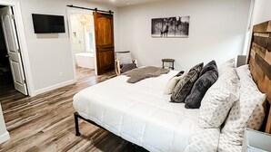 A bedroom with a large bed, a ceiling fan, a mounted TV, and a wooden floor. - Little Bear Cottage Private,Luxury Getaway!SPA! FIRE PIT! 3 MLS FROM SNP (Three Rivers)