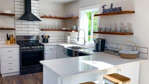 A modern kitchen with white cabinetry, a black range hood, and wooden shelves. - Little Bear Cottage Private,Luxury Getaway!SPA! FIRE PIT! 3 MLS FROM SNP (Three Rivers)