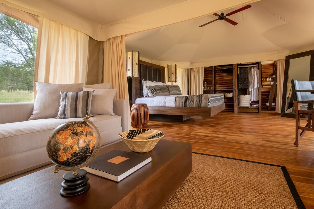 A spacious bedroom with a large bed, a bedside table with a globe and book, and a view of the outdoors.