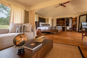A spacious bedroom with a large bed, a bedside table with a globe and book, and a view of the outdoors. - Aurari Camp (Serengeti)