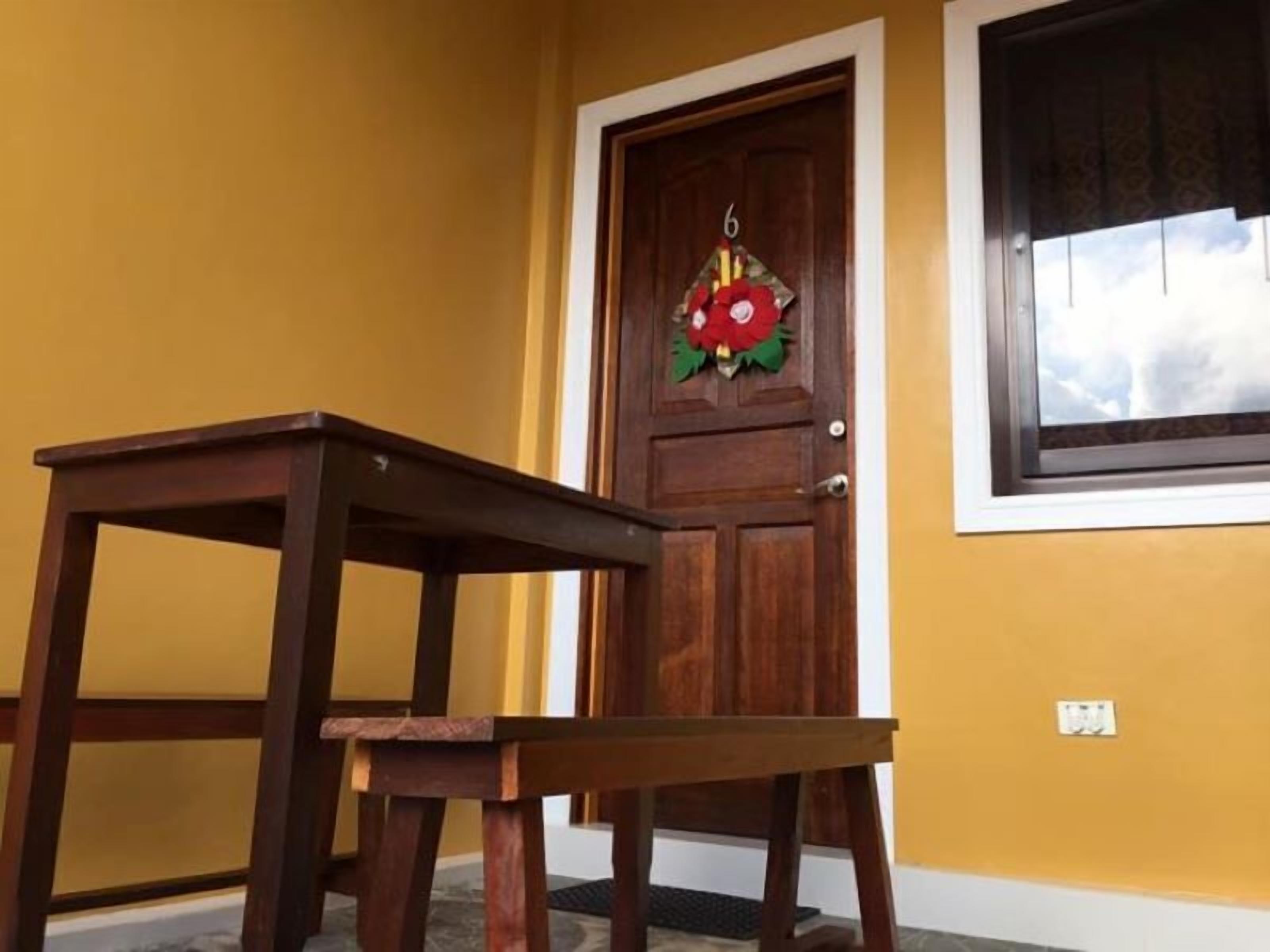 A wooden table and a door with a number 6 sign and a red flower decoration.