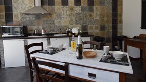 Une cuisine avec un mur recouvert de carreaux, un four à micro-ondes, un évier et un coin repas comprenant des chaises et une table mise avec de la vaisselle et une bouteille.