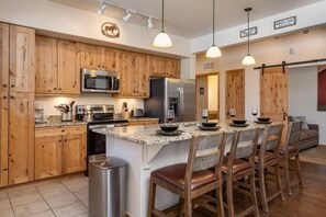 A kitchen with wooden cabinets, stainless steel appliances, a granite countertop, and a bar seating area. - Trailhead 212 Downtown walk to bars, restaurants (Winter Park)