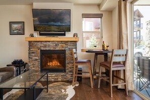 Ein Wohnzimmer mit Kamin aus Stein, einem Flachbildfernseher, einem Glastisch und einem Ledersofa.