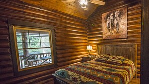 A log cabin bedroom with a bed, a window, a ceiling fan, and a painting on the wall.