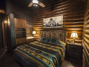 A log cabin-style bedroom with a bed, two bedside tables, a ceiling fan, and a bear painting on the wall.