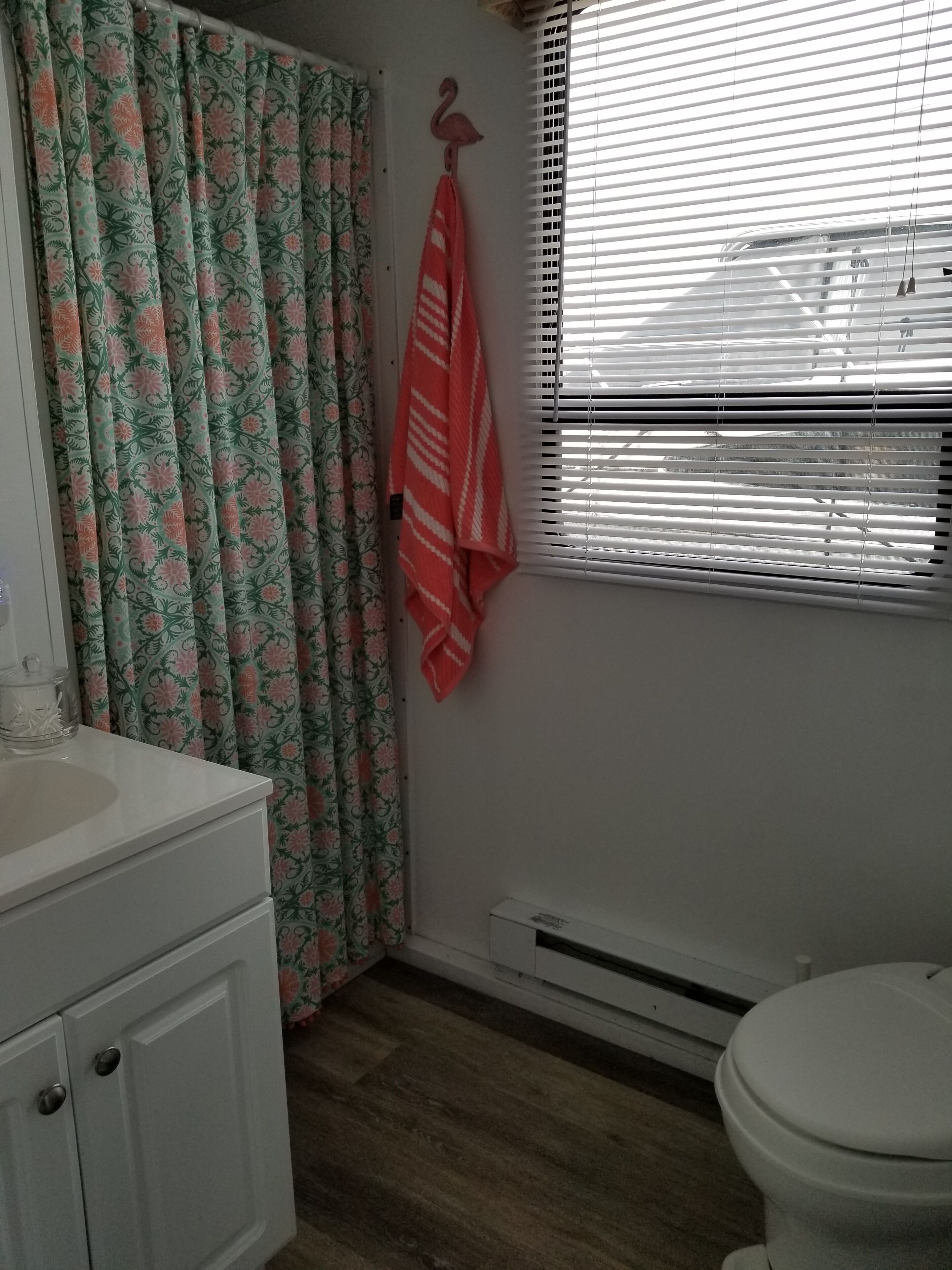 Ein Badezimmer mit einem weißen Waschbecken, einer Toilette, einem Fenster mit Jalousien und einem Duschvorhang mit Blumenmuster.