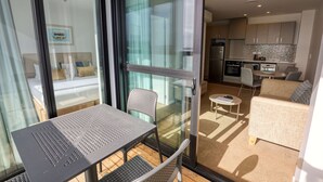 A modern living area with a glass door leading to a balcony, a small kitchen, and a seating area with a sofa and table. - Ramada Suites By Wyndham Victoria Street West (Auckland)