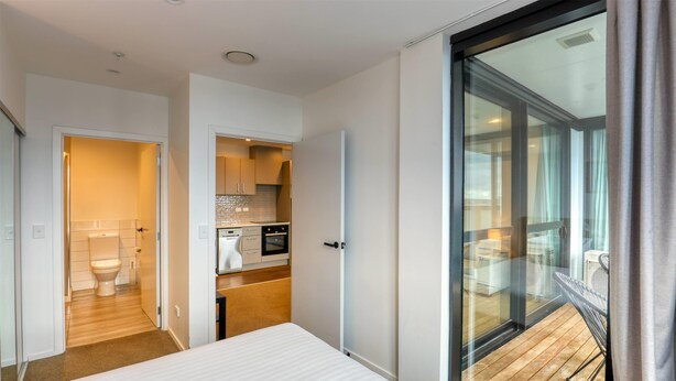 A modern hotel room with a large bed, a balcony with a wooden deck, and a kitchenette. - Ramada Suites By Wyndham Victoria Street West (Auckland)