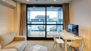 A modern hotel room with a large sliding glass door leading to a balcony, a sofa, a small table, and a TV. - Ramada Suites By Wyndham Victoria Street West (Auckland)