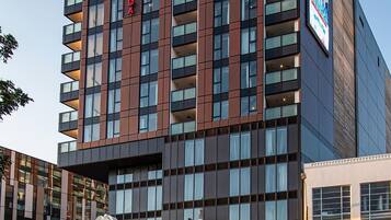 Ett modernt hotell med flera våningar, utmärkt av en tydlig skylt med texten ”RAMADA”. Fasadens design kombinerar glas och mörka paneler, och på markplan finns ett kommersiellt utrymme med en skylt som visar texten ”WINNER”.