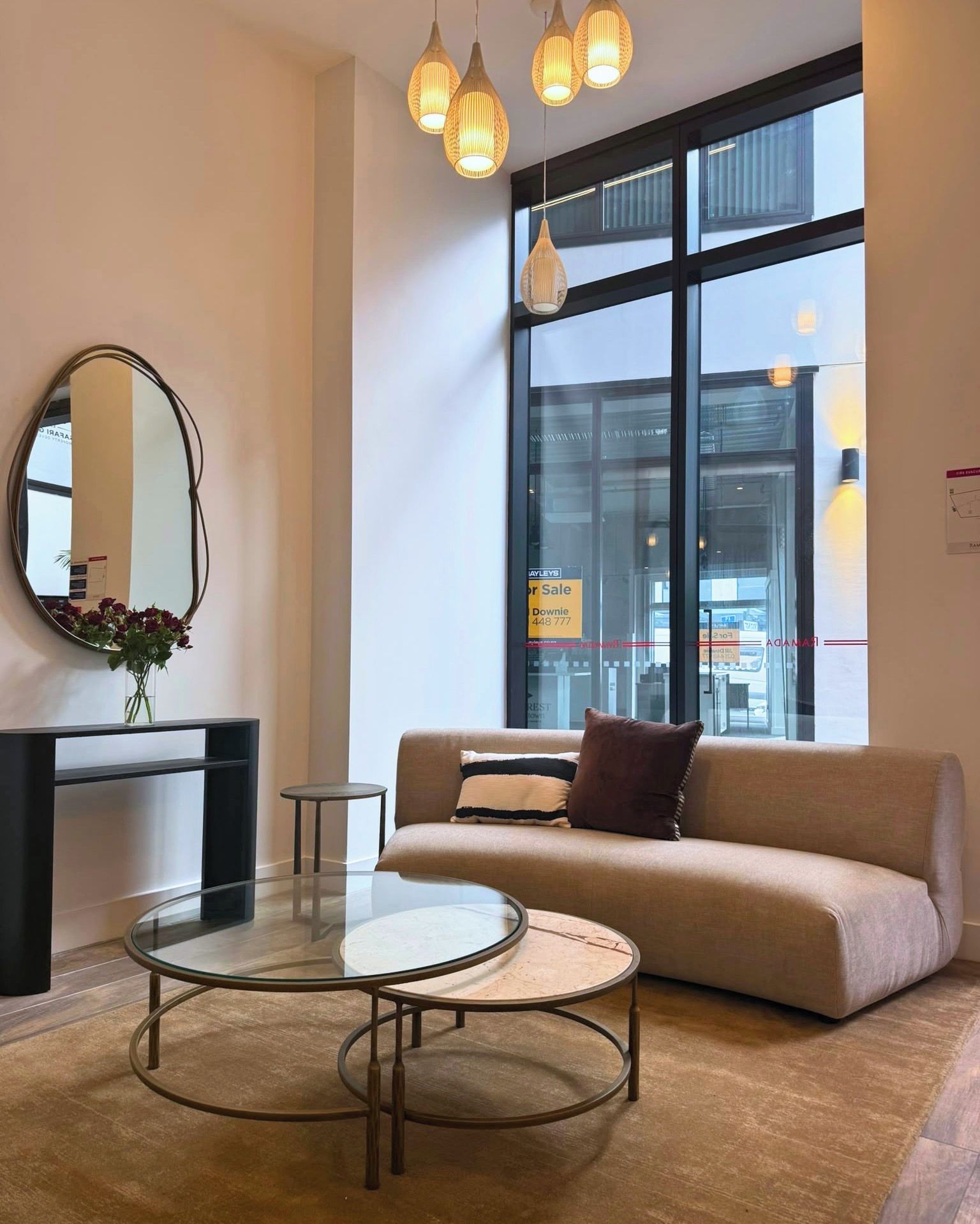 A modern living room with a sofa, a round glass coffee table, a small side table, and a mirror with flowers.