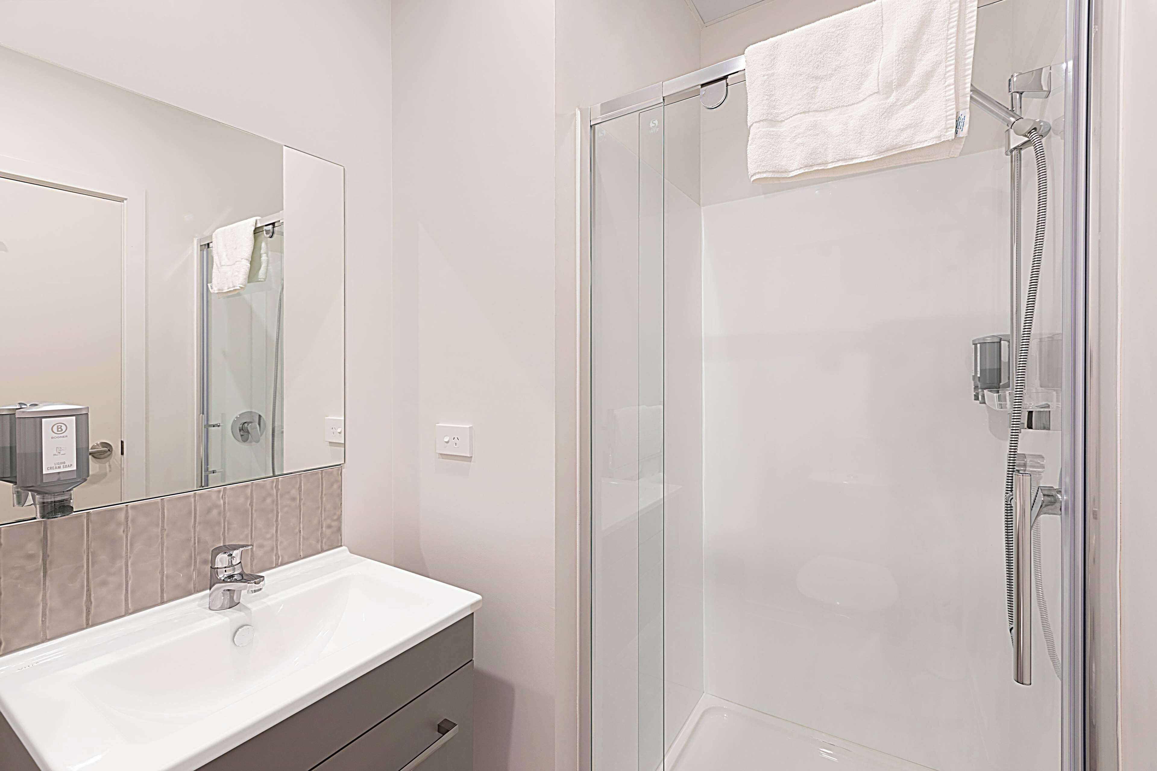 Un baño moderno con ducha de mampara de vidrio, lavamanos blanco y espejo grande.