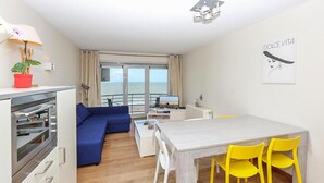 A modern room with a dining area, a sofa, a TV, and a balcony with a view of the sea. - Residentie Zeezicht, Ref 104 (Oostende)