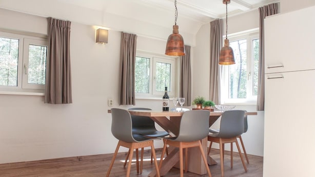 Un espace repas moderne avec une table en bois, quatre chaises grises et deux lampes suspendues.