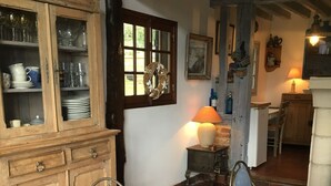 Una habitación tradicional con un armario de madera, dos sillas azules, un tapete rojo estampado y una mesita con una lámpara.