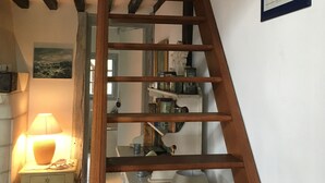 Una escalera de madera conduce a una zona superior con techo blanco y un cuadro enmarcado de un barco.