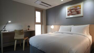 A hotel room with a large bed, a desk with a chair, a desk lamp, and a framed picture on the wall.