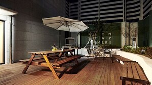 An outdoor patio with a wooden table and chairs, a large umbrella, and a sign reading "ROON STAY RIAL". - New Raon Stay (Jinju)