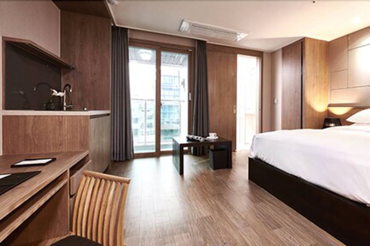 A hotel room with a bed, a desk, a chair, a small table, and a large window.
