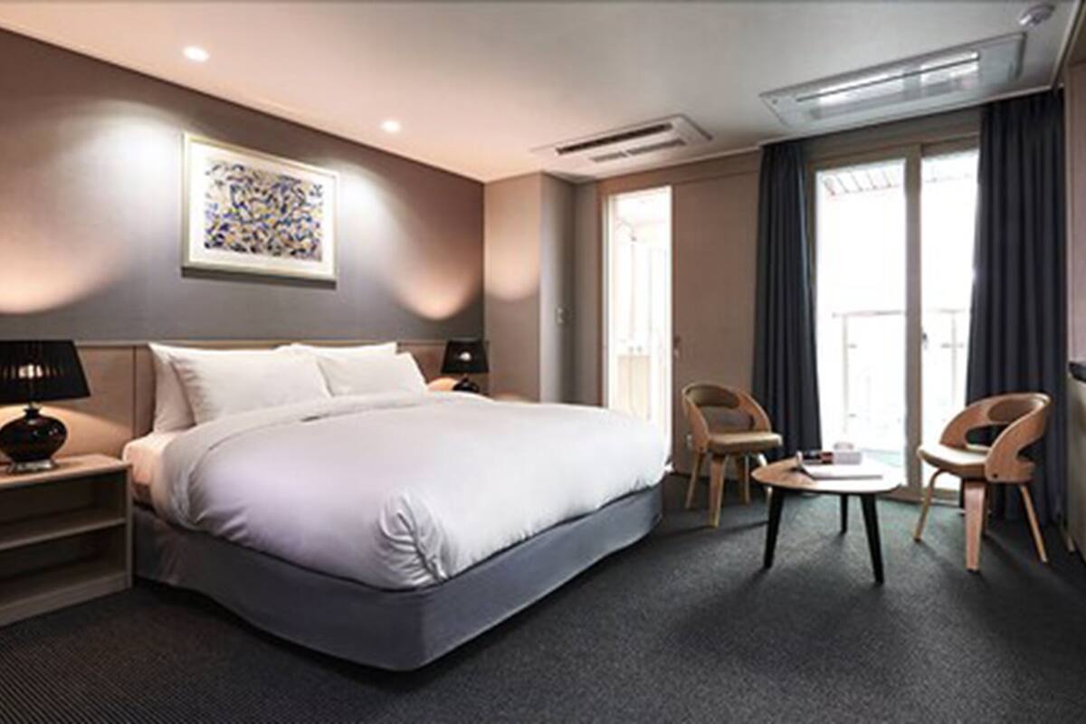 A hotel room with a large bed, two chairs, a small table, a desk, and a window with curtains.