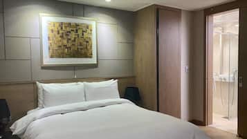 A hotel room with a large bed, a wooden headboard, a framed artwork on the wall, and a sliding door leading to a shower area.