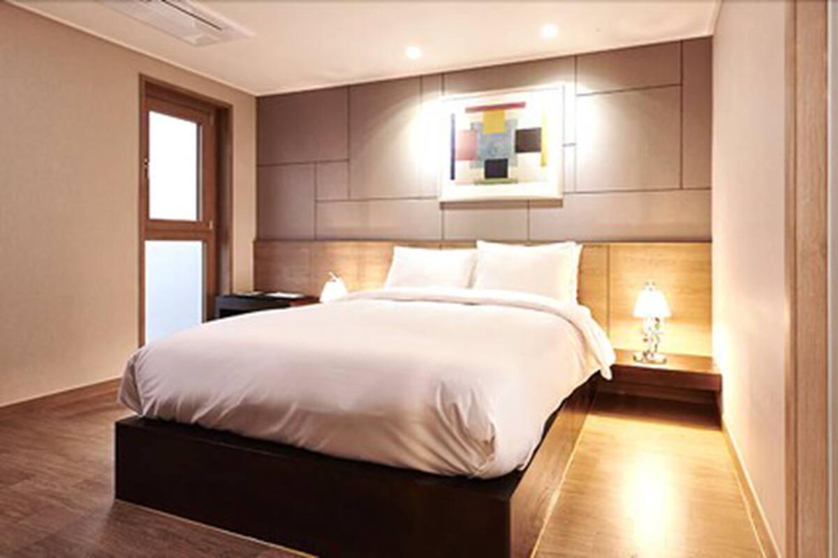 A modern hotel room with a large bed, a bedside table with a lamp, and a wall-mounted artwork.