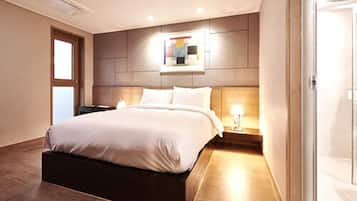 A modern hotel room with a large bed, a bedside table with a lamp, and a wall-mounted artwork.