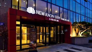 The exterior of the New Raon Stay hotel with a glass facade, a red entrance, and a signboard advertising a buffet. - New Raon Stay (Jinju)