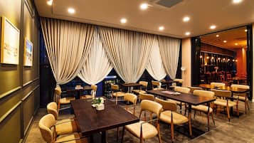 A restaurant with multiple tables and chairs, large windows with curtains, and a modern interior design.