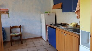 Een kleine keuken met een koelkast, fornuis en blauwe kastjes.