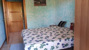 Een slaapkamer met een houten deur, een bed met een bloemenprint, een nachtkastje en een aan de muur hangend schilderij.