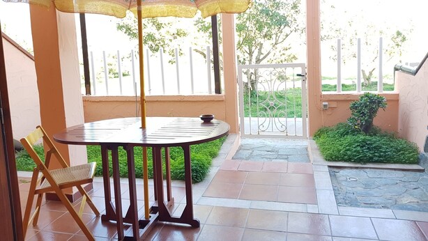 Een terras met een ronde tafel en stoelen, een parasol en een poort die naar een tuin leidt.