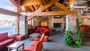 A cozy lounge area with wooden beams, stone walls, and red upholstered furniture. - Appartement près des pistes! Piscine + Sauna (La Toussuire)