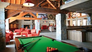 A pool table with balls, red chairs, and a fireplace in a wooden room with stone pillars. - Appartement près des pistes! Piscine + Sauna (La Toussuire)