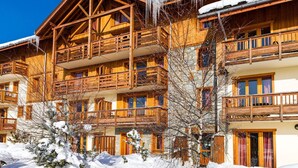 A wooden chalet with balconies, snow-covered surroundings, and a clear blue sky.