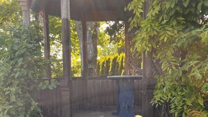 A wooden gazebo with a bench, surrounded by greenery and trees.