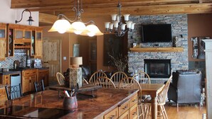 A spacious kitchen with a large island, wooden ceiling beams, and a stone fireplace.