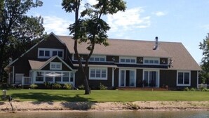 A two-story house with a large front porch, a covered patio, and a view of a lake.