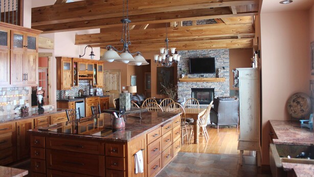 A spacious kitchen with wooden cabinets, a large island, and a stone fireplace.