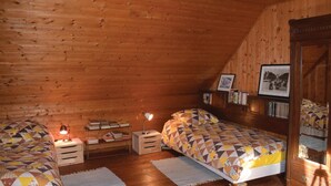 A cozy attic bedroom with wooden walls, two beds with patterned quilts, a small desk with books, and a framed photo on the wall. - 2 bedroom pet friendly home in Plourivo (Plourivo)