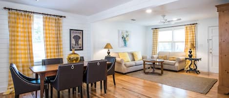A living room with a dining area, wooden flooring, and yellow curtains.