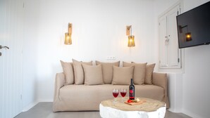 A modern living room with a beige sofa, two wall-mounted lamps, a flat-screen TV, and a small round coffee table with wine glasses and a bottle. - VILLA AGAPITOS (naxos)