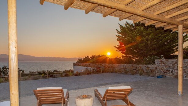 A wooden pergola with two lounge chairs and a round table, overlooking a scenic sunset view of the sea. - VILLA AGAPITOS (naxos)