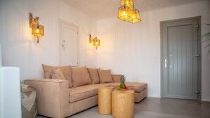 A modern living room with a beige sectional sofa, two wooden side tables, and a fruit bowl on one table. - VILLA AGAPITOS (naxos)